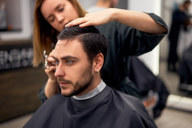 Cabeleireiro mulher cortar cabelo bonito homem caucasiano na barbearia moderna