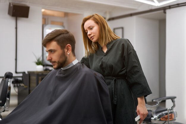 Cliente do sexo feminino feliz usando secador de cabelo no salão de  cabeleireiro. mulher sentada na cadeira no hairsalon. negócios de moda e  beleza, serviços profissionais
