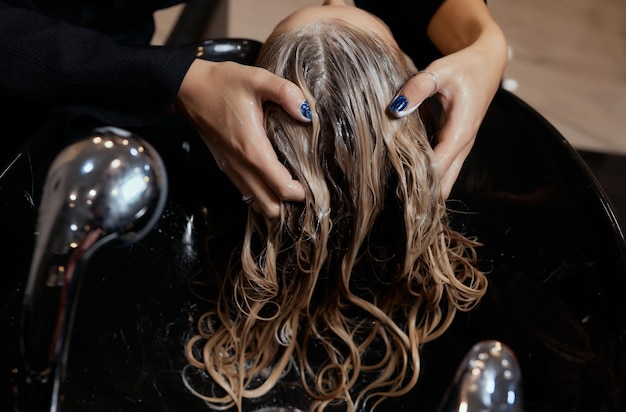 Cabeleireiro no salão de beleza lava o cabelo do cliente antes do procedimento de aplicação de ingredientes naturais restauradores e vitaminas ao cabelo e corte de cabelo