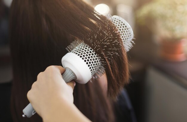 Cabeleireiro penteando longos cabelos castanhos com escova redonda em salão de beleza