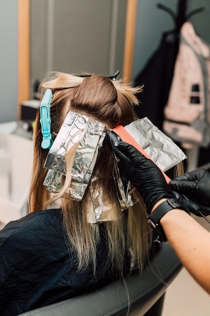 Foto cabeleireiro penteando uma mecha de cabelo loiro tingido com um pente