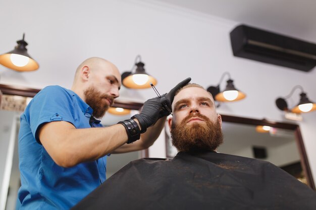 Cabeleireiro profissional atendendo cliente, barbeando uma barba espessa com navalha reta