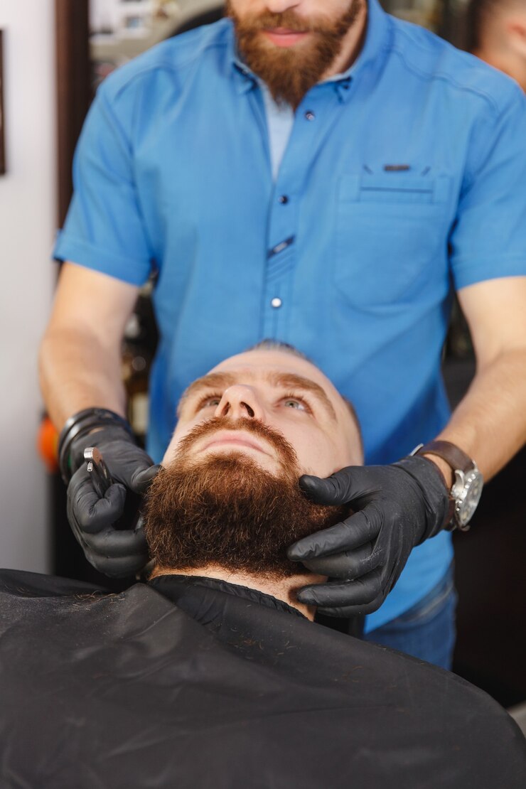 Foto cabeleireiro profissional atendendo cliente, barbeando uma barba espessa com navalha reta