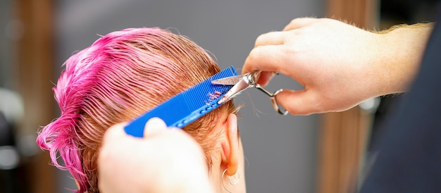 Cabeleireiro profissional está cortando cabelo curto rosa com uma tesoura em um salão de cabeleireiro de perto.