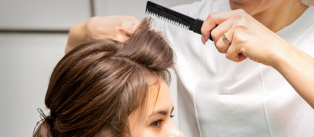 Cabeleireiro profissional fazendo penteado para uma bela morena jovem com cabelo comprido. Conceito de moda e beleza.