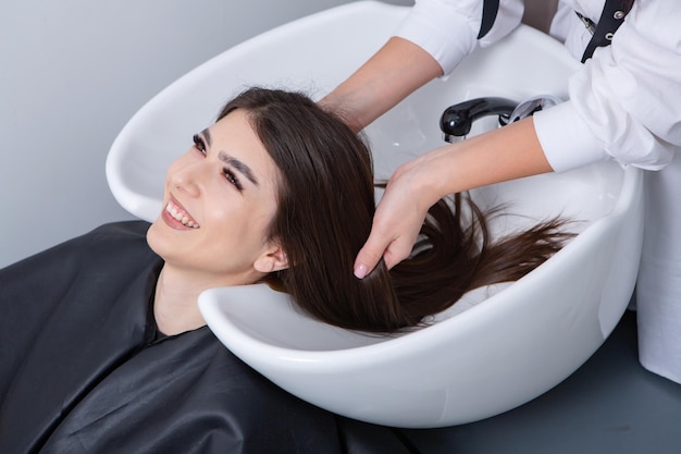 Foto cabeleireiro profissional lavando cabelo de jovem no salão de beleza