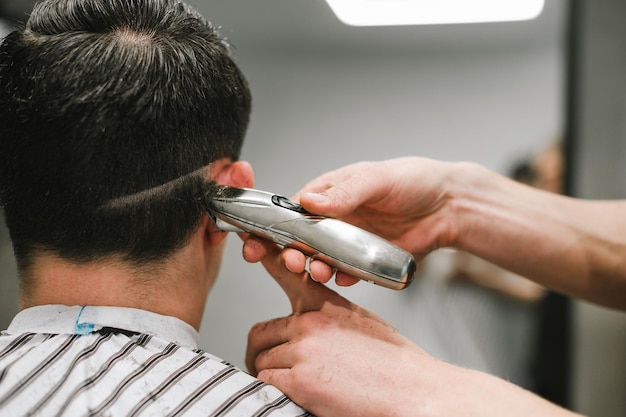 Cabeleireiro profissional masculino faz penteado para cliente no processo de foto de closeup de barbearia