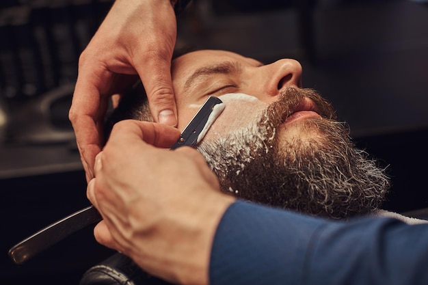 Cabeleireiro profissional modelando a barba na barbearia. Foto em close.