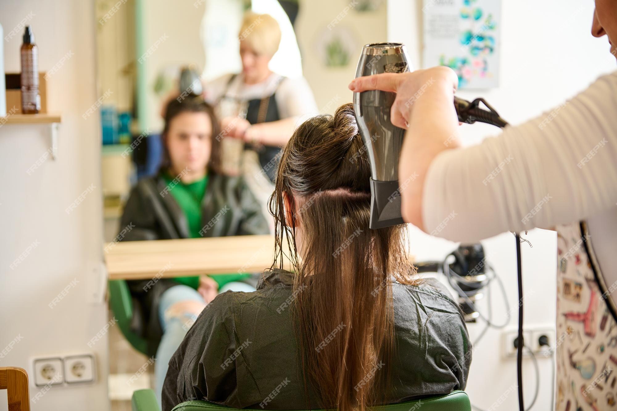 Secagem de cabelo no estúdio de cabeleireiro. estilista de cabeleireira  seca o cabelo com secador de cabelo e escova redonda ruiva de uma mulher em  um salão de beleza.