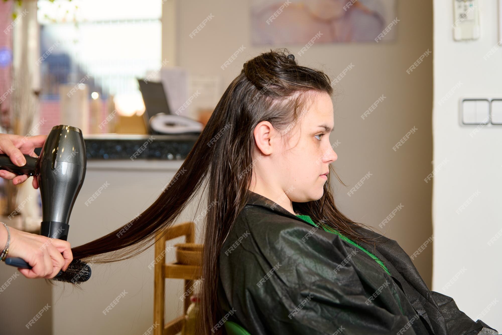 Cabeleireiro seca e modela o cabelo com um secador de cabelo no salão de  beleza