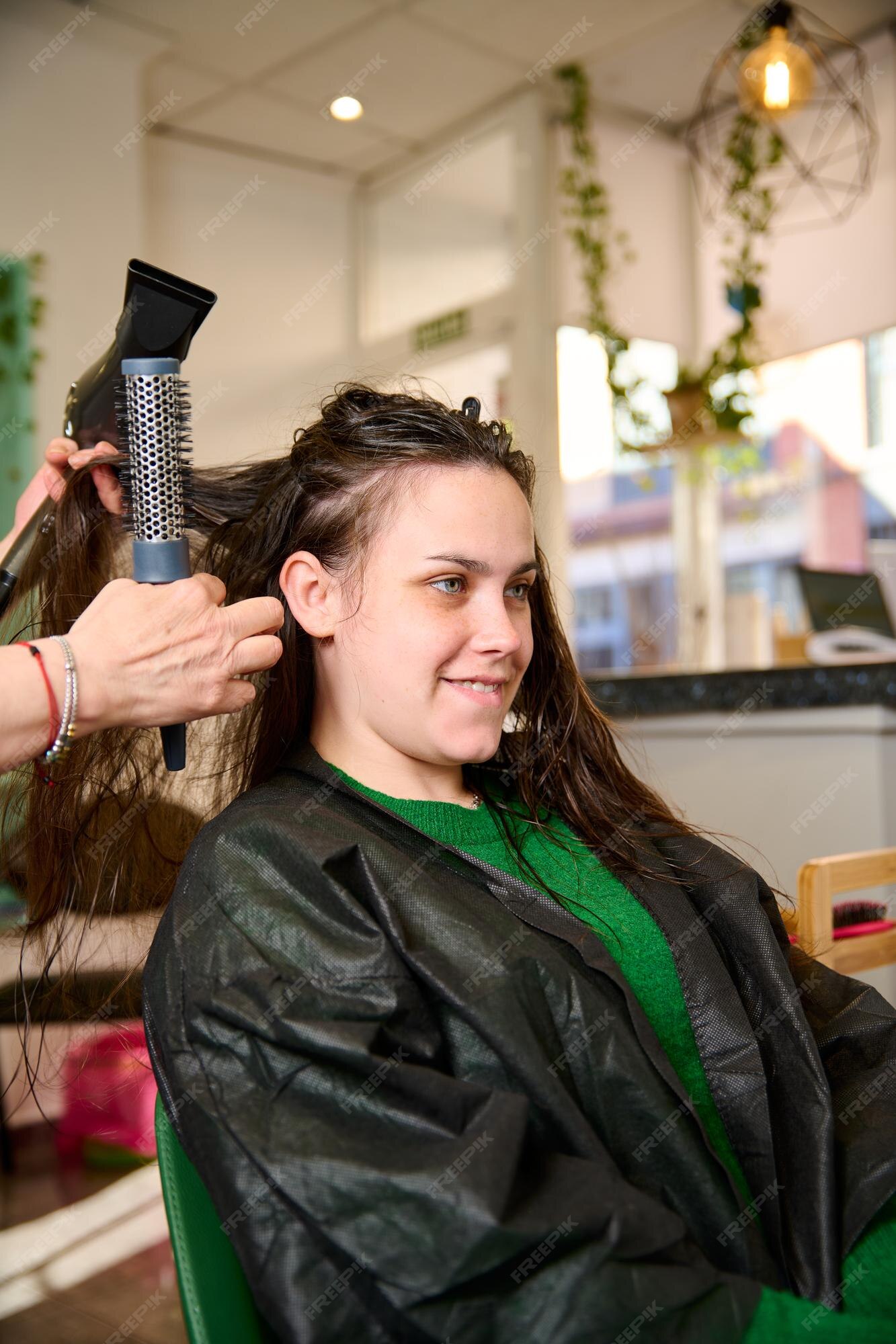 Cabeleireiro seca e modela o cabelo com um secador de cabelo no salão de  beleza