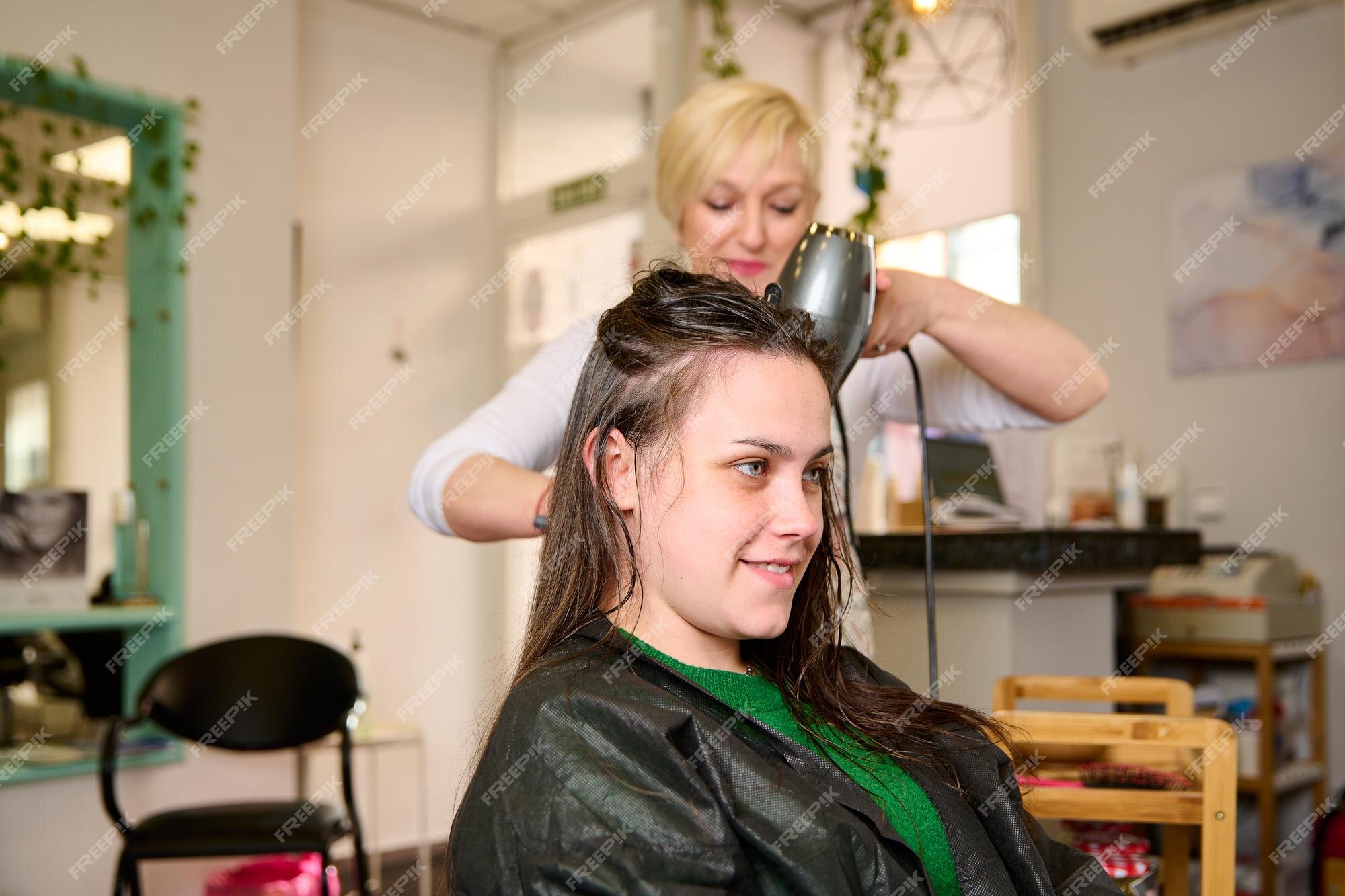 Cabeleireiro seca e modela o cabelo com um secador de cabelo no salão de  beleza