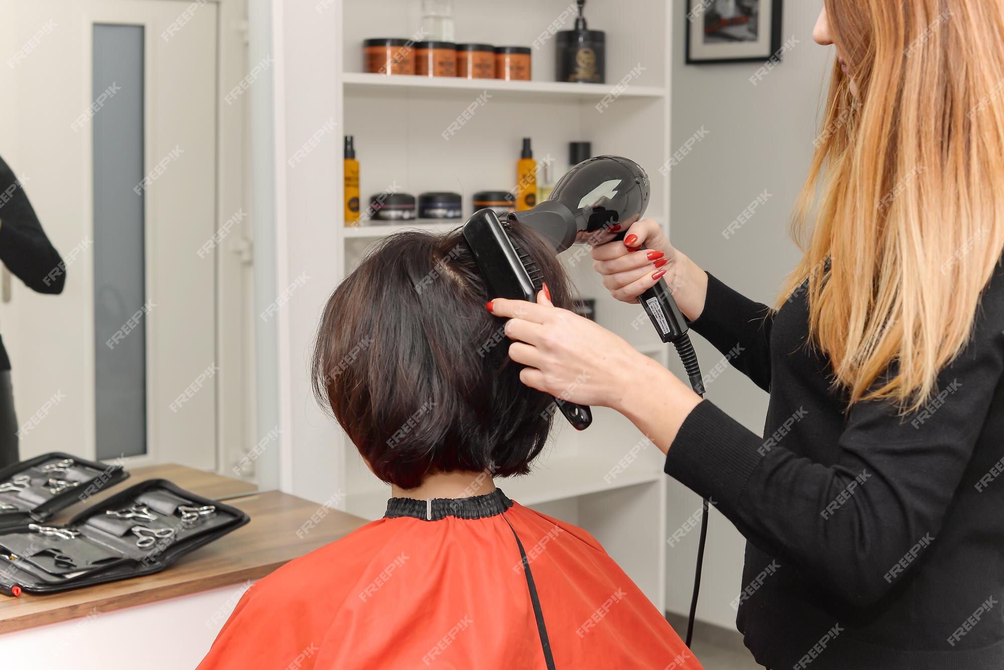 Cabeleireiro seca o cabelo com secador de cabelo para uma mulher