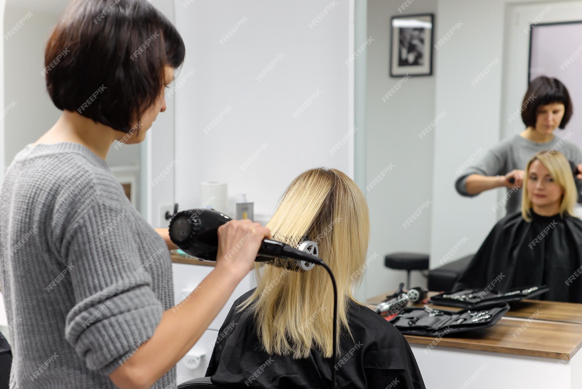 Cabeleireiro seca o cabelo com secador de cabelo para uma mulher após um  corte de cabelo no salão