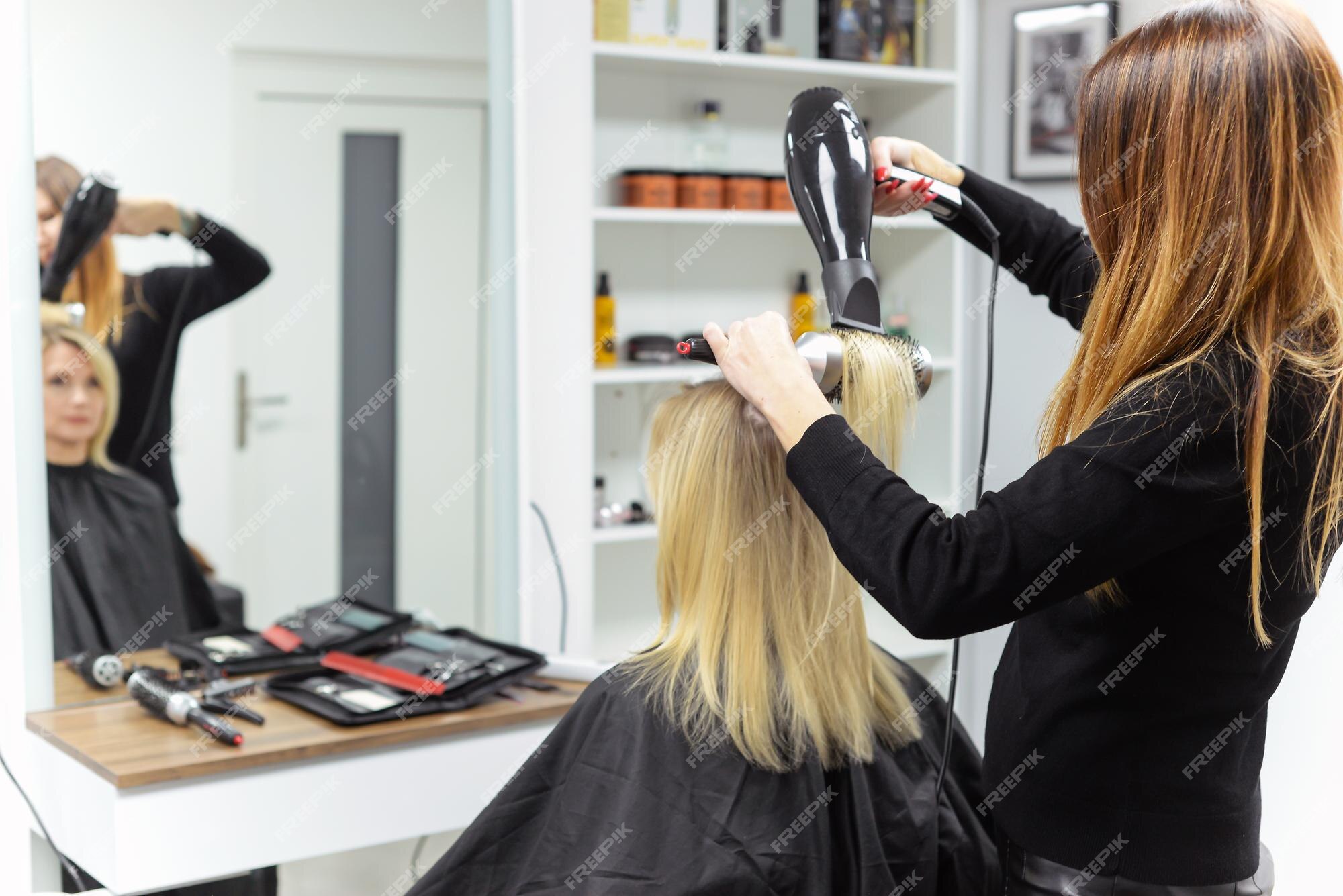 Cabeleireiro seca o cabelo com secador de cabelo para uma mulher