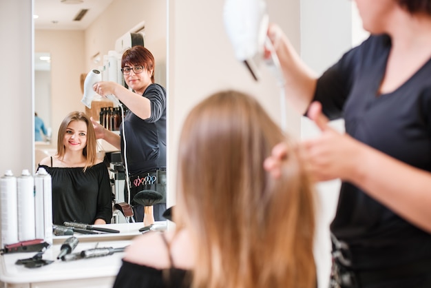 Cabeleireiro seca e modela o cabelo com um secador de cabelo no salão de  beleza