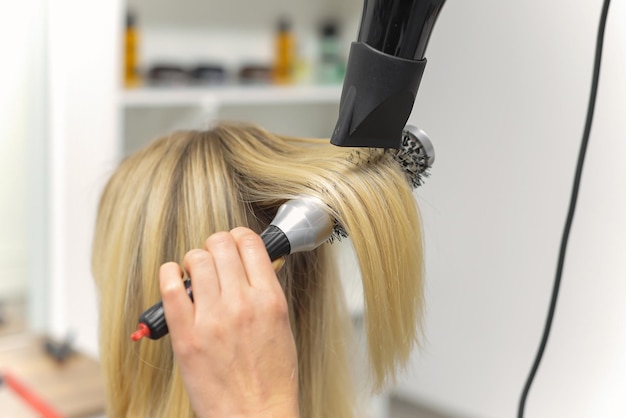 Cabeleireiro seca o cabelo com uma mulher de secador de cabelo no