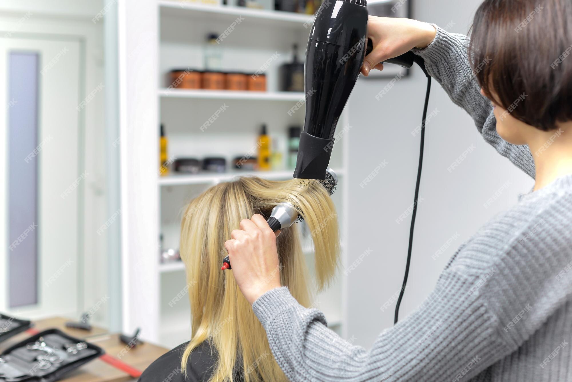 Cabeleireiro seca o cabelo com secador de cabelo para uma mulher