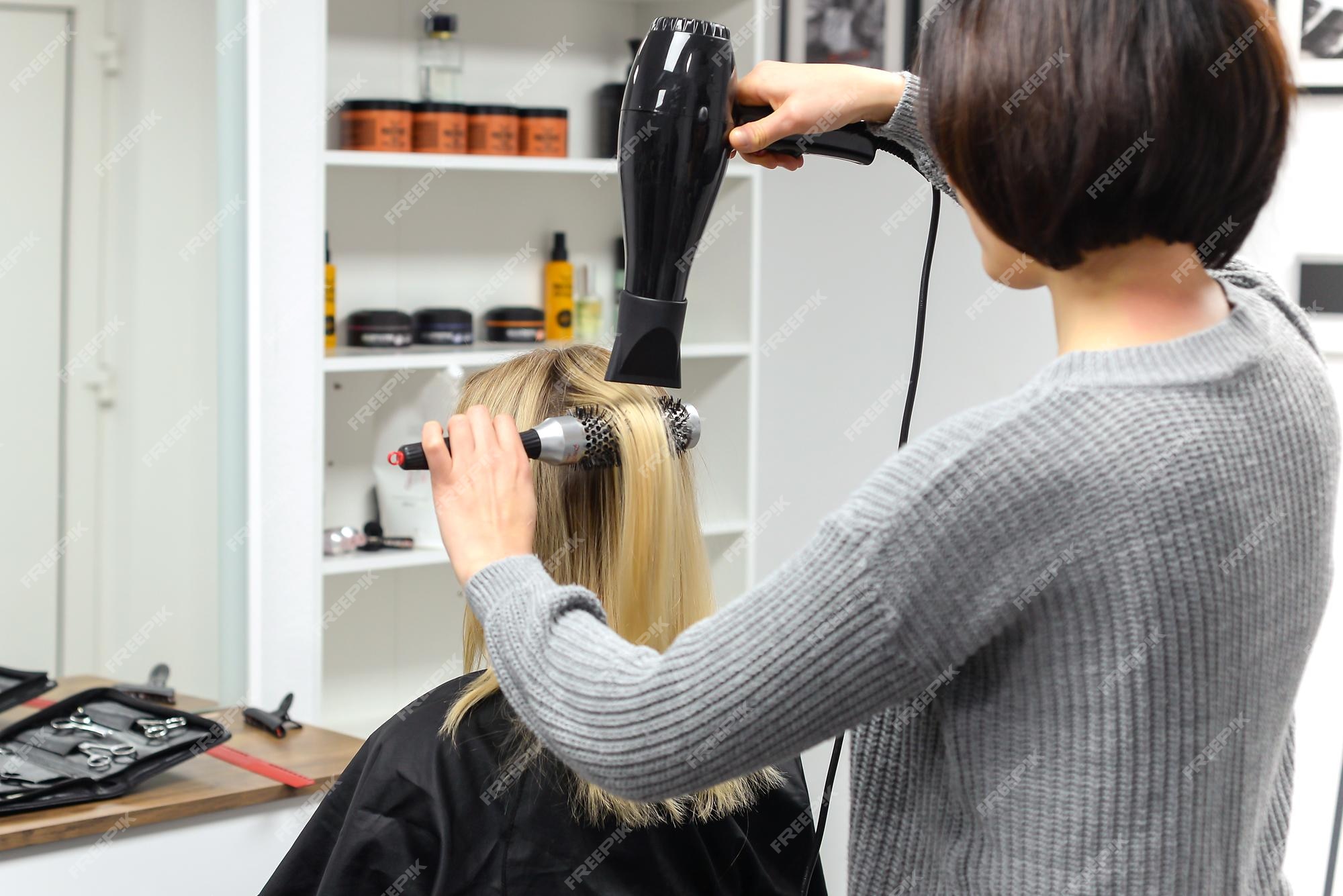 Cabeleireiro seca o cabelo com secador de cabelo para uma mulher após um  corte de cabelo no salão