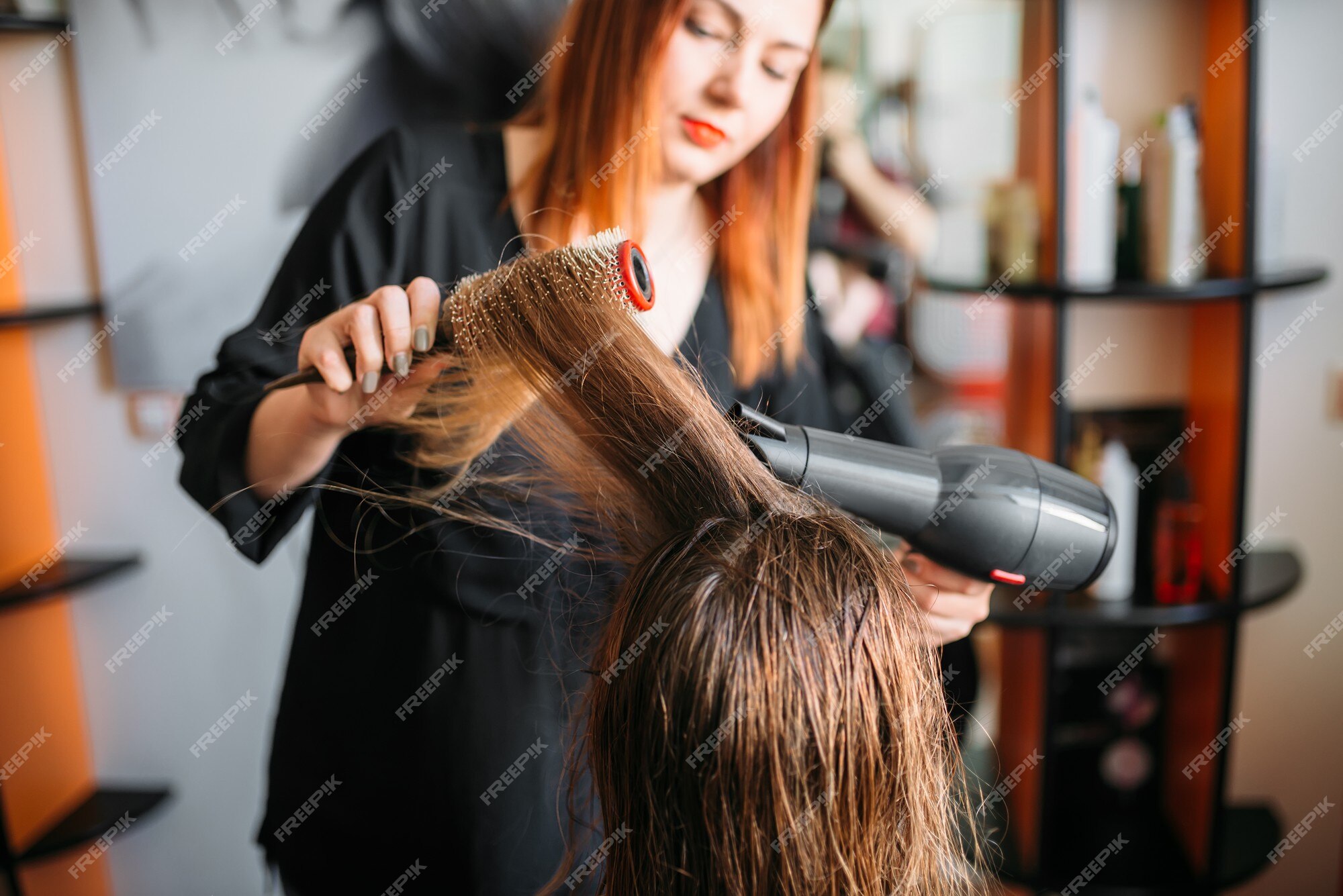 Secagem de cabelo no estúdio de cabeleireiro. estilista de cabeleireira  seca o cabelo com secador de cabelo e escova redonda ruiva de uma mulher em  um salão de beleza.