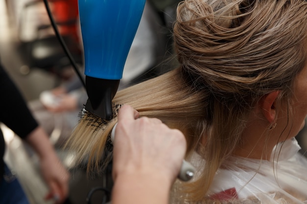Cabeleireiros secando cabelos louros com secador e escova redonda