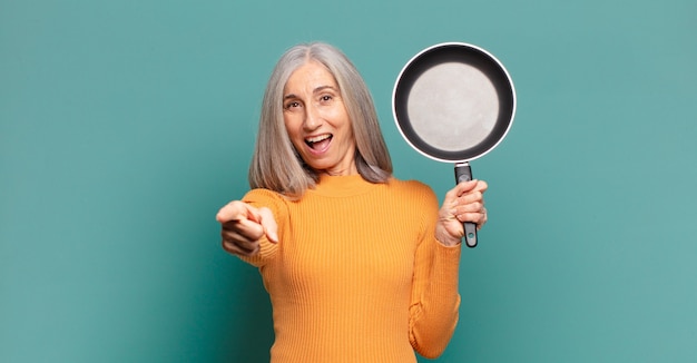 Cabello gris bastante mujer de mediana edad aprendiendo a cocinar con una sartén