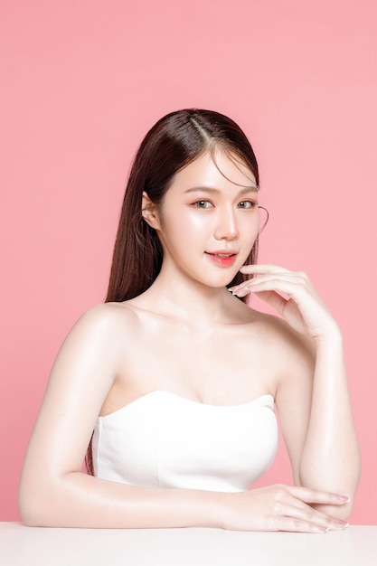 El cabello largo de una joven asiática con maquillaje natural en la cara tiene labios carnosos y una piel limpia y fresca sobre un fondo rosa aislado Retrato de una linda modelo femenina en el estudio Tratamiento facial Cosmetología