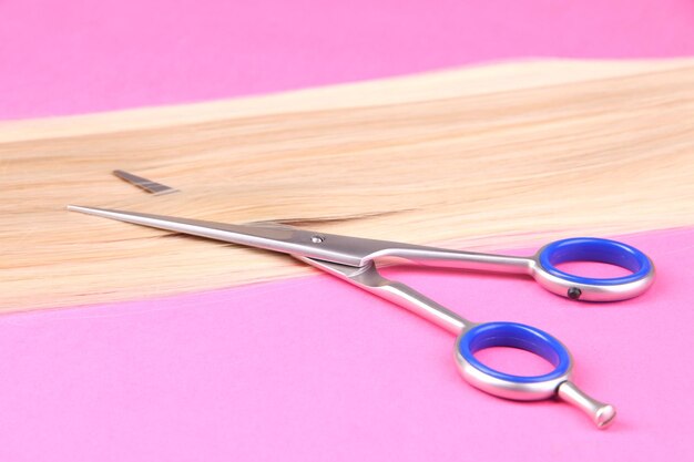 Foto cabello largo y rubio con tijeras sobre fondo rosa