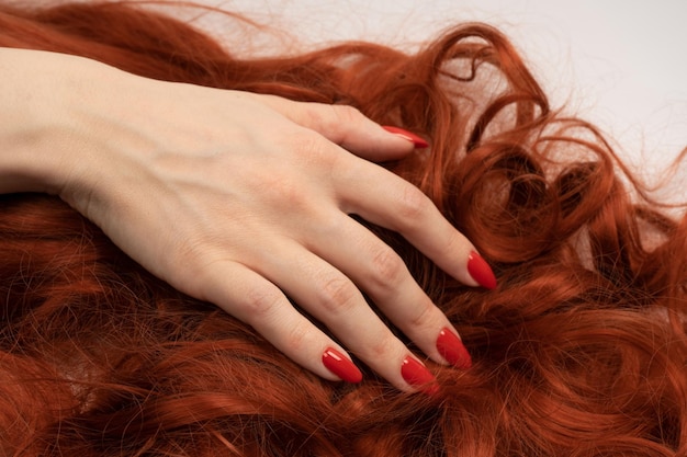 Cabello rizado rojo en manos de mujer con uñas rojas