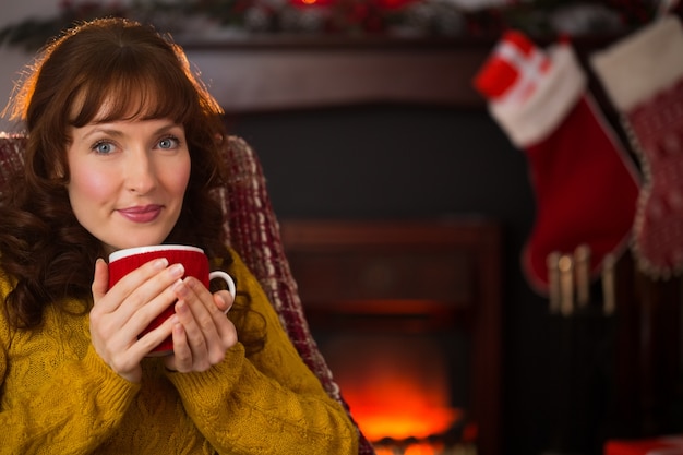 Cabello rojo sonriente disfrutando de bebida caliente en Navidad