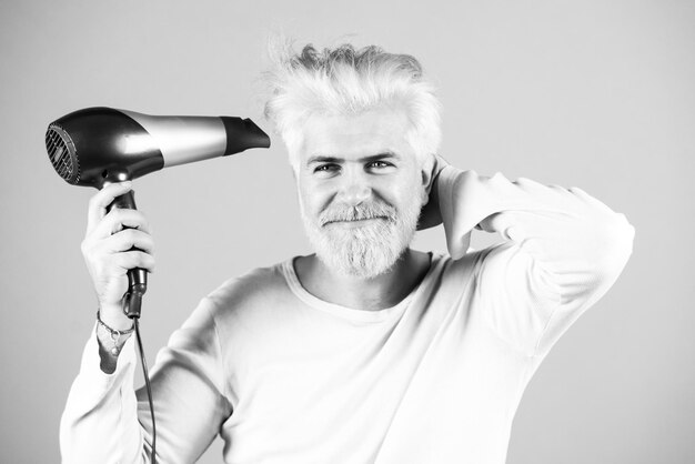 Cabello rubio barbudo seco. Un hombre guapo con el pelo largo se seca el pelo con un secador de pelo.