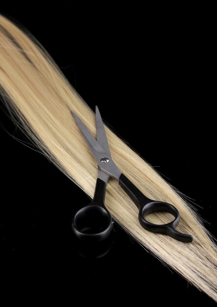Cabello rubio brillante y tijeras para cortar el cabello aisladas en negro