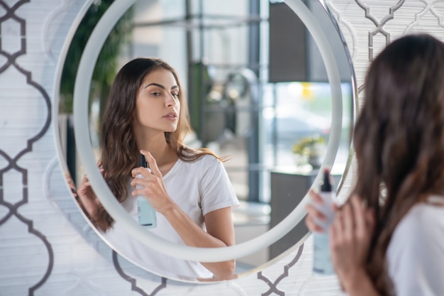 Cabello sano y hermoso. Una mujer usando una laca para el cabello cerca del espejo.