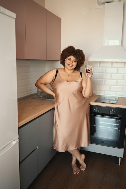 Cabelo afro bonito e curvilíneo plus size mulher negra africana bebendo vinho tinto em estilo escandinavo moderno