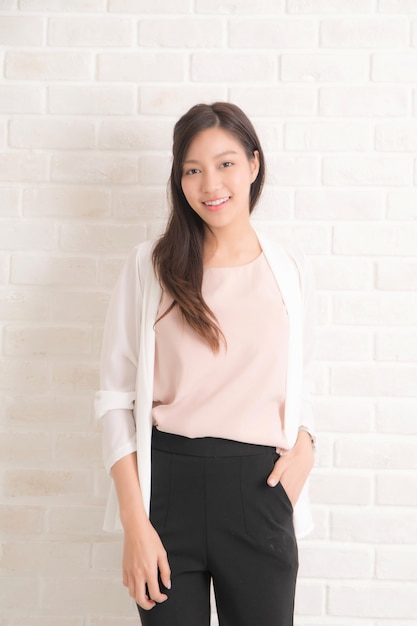 Cabelo castanho comprido de linda mulher bonita asiática, sorrindo e virada para a vista lateral com uma camiseta preta e jeans em pé positng na parede bege.