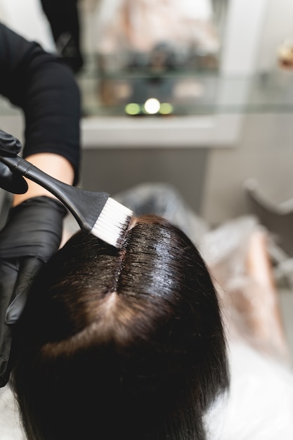 Cabelo colorido. menina morena gentil sentada em frente ao espelho enquanto olha para seu reflexo durante o procedimento de beleza