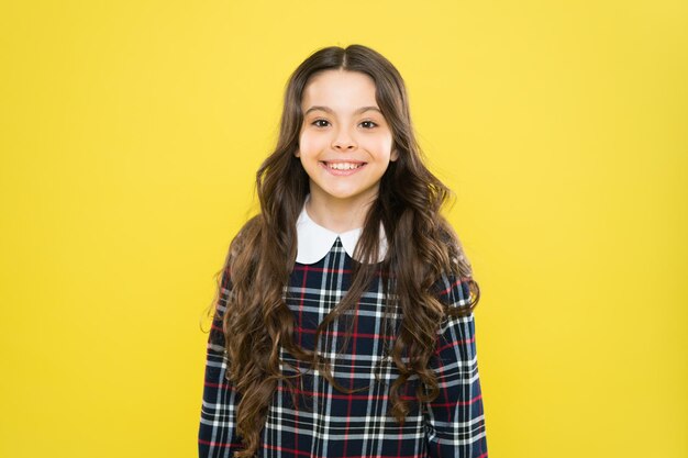 Cabelo como fogo de volta à escola pequena menina vestido xadrez elegante conceito de moda infantil se preocupe com o cabelo criança tem cabelos longos e encaracolados após a visita ao cabeleireiro estudante feliz em uniforme elegante