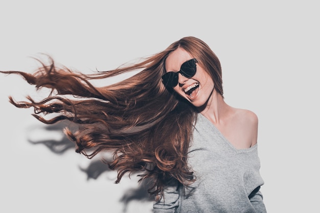 Cabelo como fogo. Mulher jovem e atraente sorridente com óculos escuros e cabelo despenteado, olhando para longe em pé