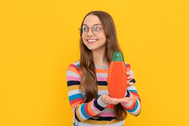 Foto cabelo comprido de criança alegre em óculos mostrando publicidade de garrafa de gel de banho