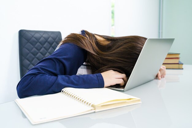 Cabelo comprido de mulher jovem adormecer na mesa com o laptop