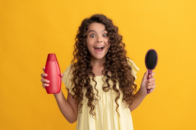 Cabelo encaracolado de criança chocada segura pente e garrafa de xampu penteado de beleza adolescente