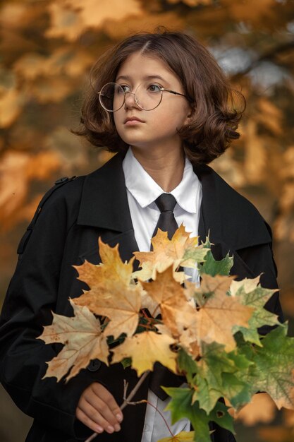 Cabelo encaracolado em óculos adolescente segurando galho com folhas de bordo de outono na floresta