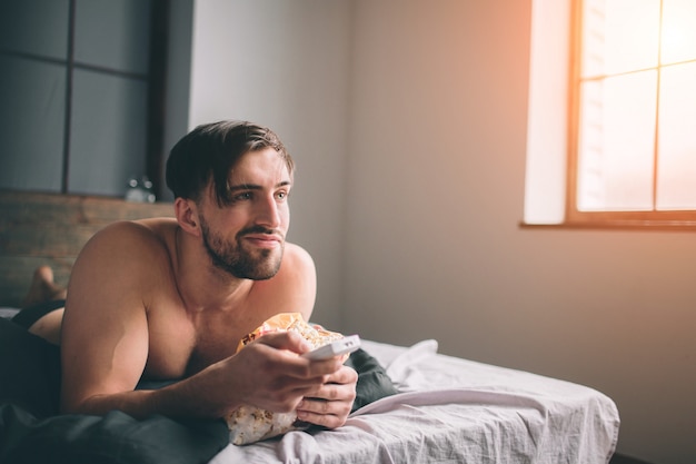 Cabelo escuro barbudo nu assistindo televisão deitado na cama