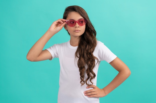 Cabelo longo cacheado de menina adolescente séria em estilo casual de óculos de sol sobre fundo azul, estilo de verão.