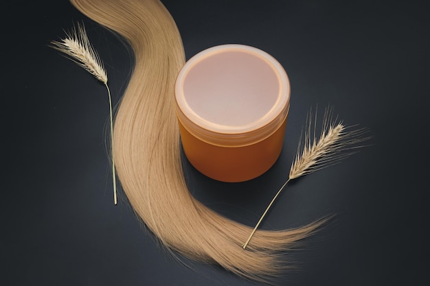 Cabelo longo loiro com frasco de creme e galhos de trigo maduro Cabelo saudável Conceito de equipamentos de salão de cabeleireiro tesouras de cabeleireiro premium Acessórios para corte de cabelo