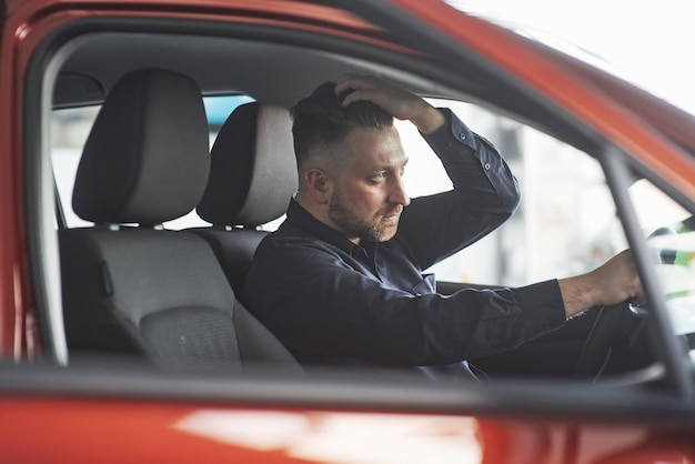 Cabelo moderno Homem de roupa oficial a experimentar o seu novo carro no salão de automóveis