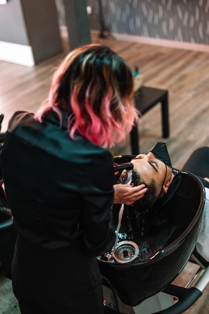 Cabelo rosa elegante lavando cabelos de clientes em salão de beleza