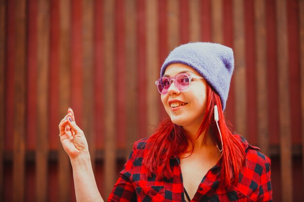 Cabelo vermelho de menina de beleza jovem ouve música em fones de ouvido e dança na rua da cidade. Menina elegante com óculos de sol rosa curtindo música