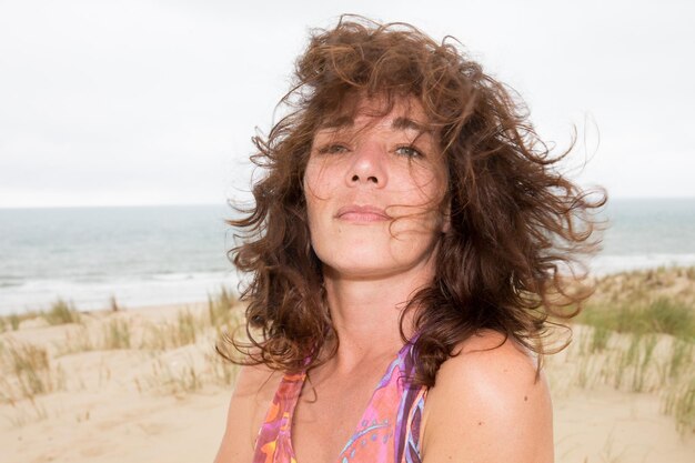 Cabelos no vento mulher de meia idade sentada na praia sorrindo no verão