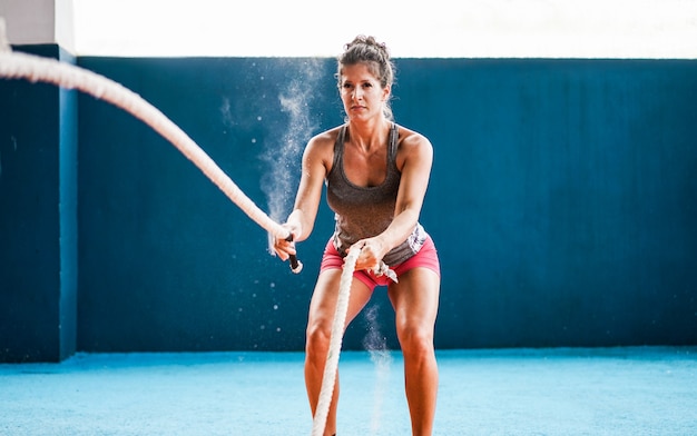 Caber mulher com corda de batalha no ginásio de fitness